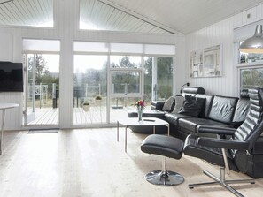 A modern living room with a black leather sofa, a glass door leading to an outdoor deck, and a flat-screen TV mounted on the wall. - 4 Star Holiday Home in Juelsminde (Juelsminde)