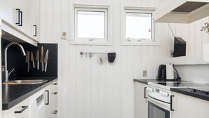 A modern kitchen with white cabinetry, a black countertop, a sink, a stove, and two windows. - 4 Star Holiday Home in Juelsminde (Juelsminde)