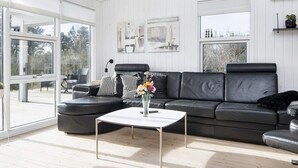 A modern living room with a black leather sofa, a white coffee table, and a large window providing a view of the outdoors. - 4 Star Holiday Home in Juelsminde (Juelsminde)