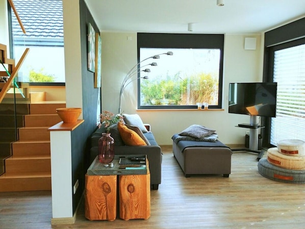 A modern living room with a staircase, a sofa, a coffee table, and a television. - Holiday House House on Muhlfeldsee (Lobnitz)