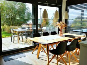 Een moderne eetruimte met een glazen tafel en stoelen, een vaas met bloemen en uitzicht op het omliggende landschap.