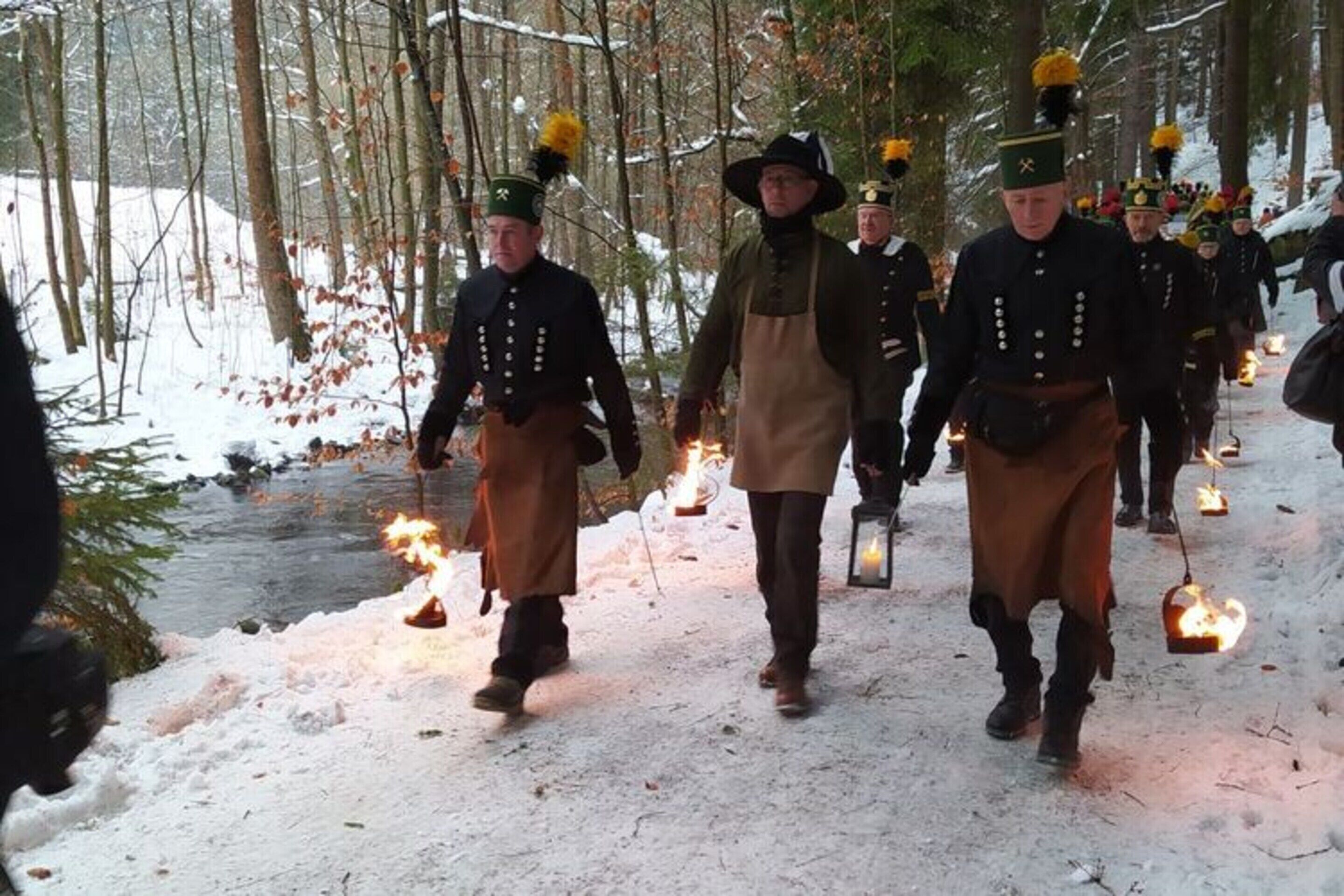 A group of people in historical costumes walking through a snowy forest.