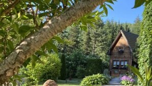 Une cabane en bois avec un toit en pente, entourée d’un jardin bien entretenu et d’arbres.