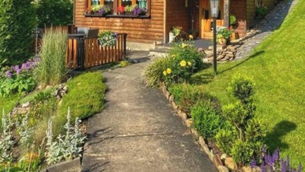 Une cabane en bois avec un toit en pente, un porche à l’avant et un chemin de jardin menant à l’entrée.