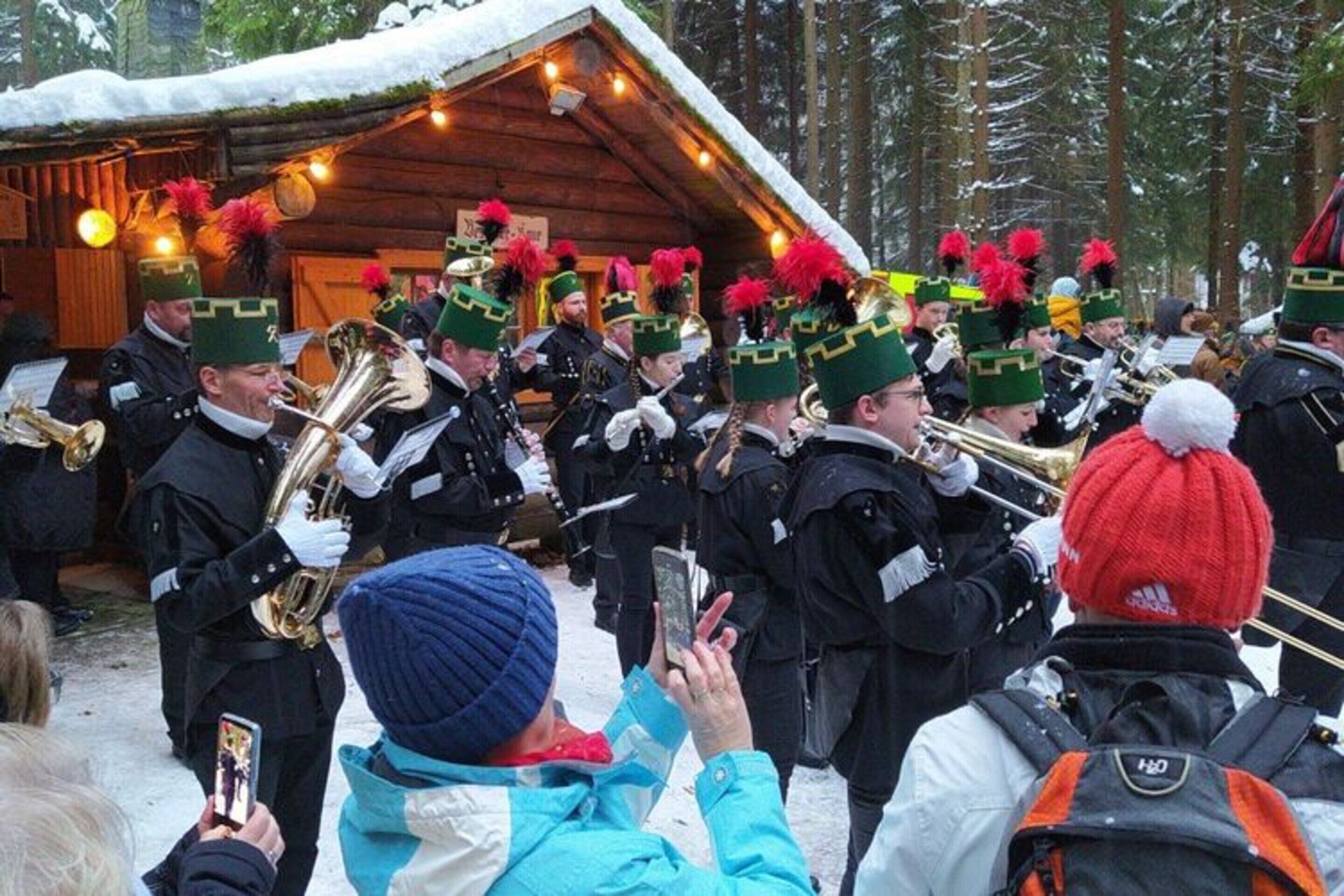 A group of musicians in uniform with hats and feather decorations, performing outdoors in a snowy setting.