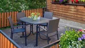 Une cabane en bois avec une table et des chaises sur une terrasse, entourée d’une clôture en bois et d’une végétation luxuriante.