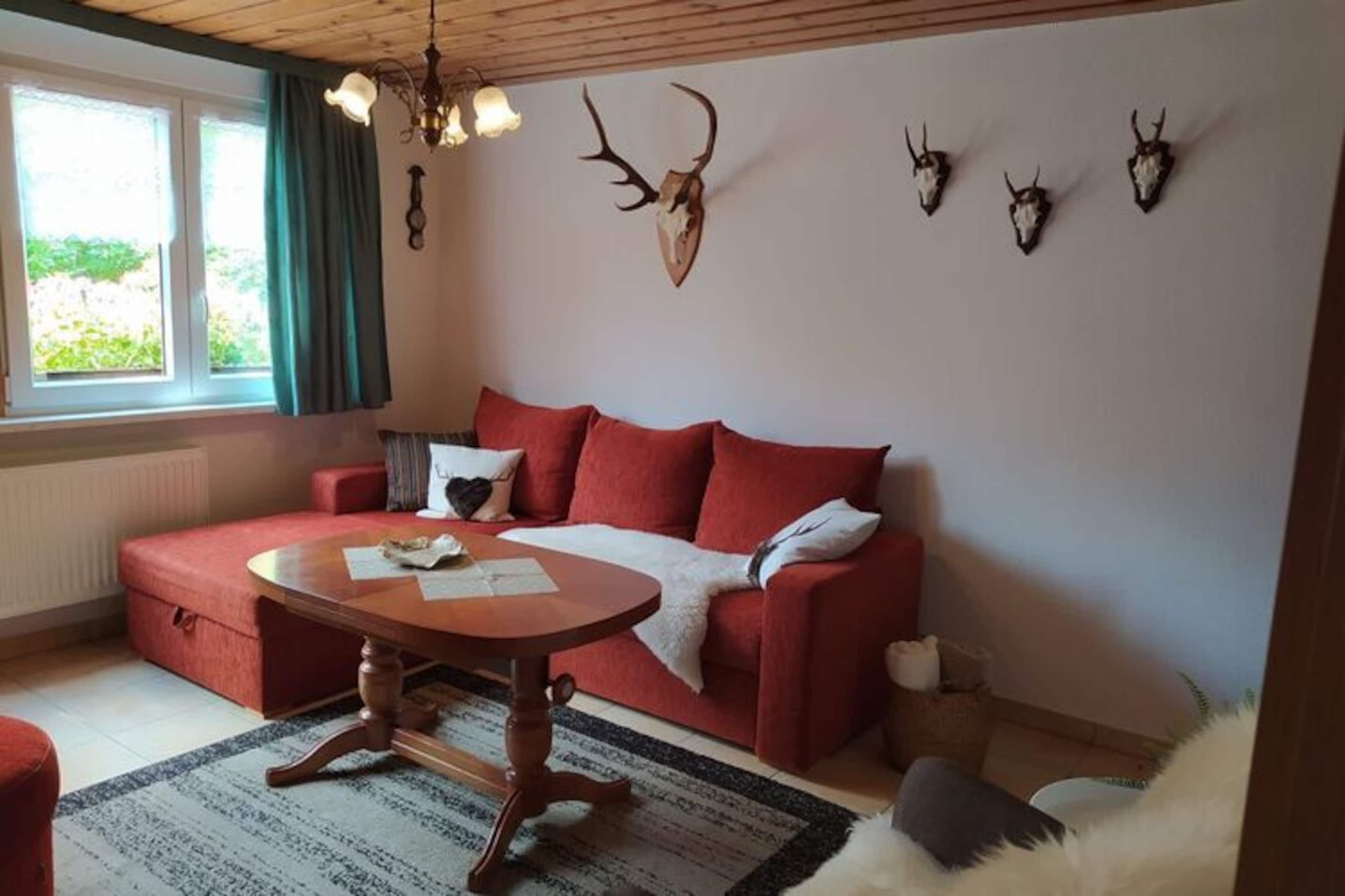 A cozy living room with a red sofa, a wooden coffee table, and a window with curtains.