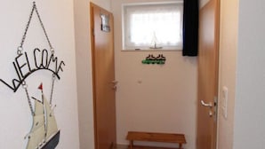 A hallway with a welcome sign, a bench, and a window with a sailboat decoration. - Wattloper Right Comfortable Holiday Residence (Wittmund)
