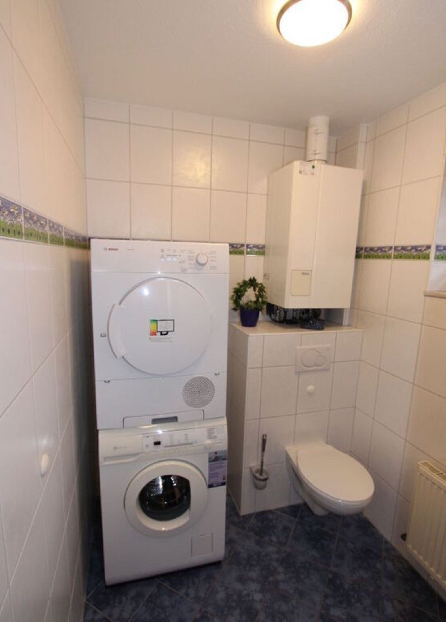 Un baño pequeño con lavadora de carga frontal, inodoro y un mueble pequeño sobre el inodoro.