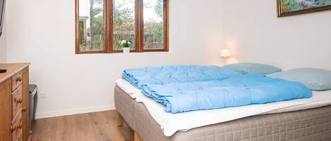 Un dormitorio con cama, ventana con vista a árboles, lámpara y un cuadro en la pared.