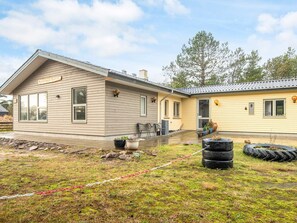 A two-story house with a covered porch, a small outdoor seating area, and a yard with a tire planter. - 8 Person Holiday Home in Blavand (Blavand)