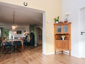 A spacious dining area with a wooden table and chairs, a black cabinet with glass doors, and a white door. - 8 Person Holiday Home in Blavand (Blavand)
