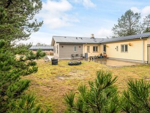 A two-story house with a covered patio, a small garden with pine trees, and a garage. - 8 Person Holiday Home in Blavand (Blavand)
