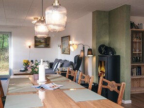 A modern living room with a wooden dining table, comfortable seating, a fireplace, and a bookshelf. - 8 Person Holiday Home in Blavand (Blavand)