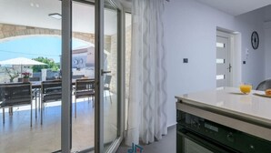 A modern kitchen with a sliding glass door leading to an outdoor dining area. - Grande Comfortable Holiday Residence (Svetvincenat)