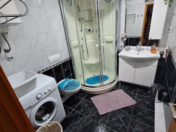 Une salle de bain avec une douche à parois de verre, un lavabo, des toilettes et un lave-linge.