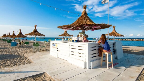 A beachside bar with thatched umbrellas, a tiled floor, and a view of the sea. - Residence With Swimming Pool Nearby the sea (Rimini)