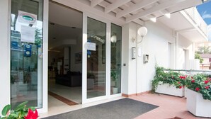A hotel entrance with a glass door, a reception desk, and a small outdoor area with steps and potted plants. - Residence With Swimming Pool Nearby the sea (Rimini)