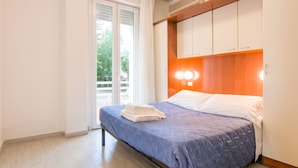 A bedroom with a bed, a window with curtains, a wooden headboard, and a wall-mounted light. - Residence With Swimming Pool Nearby the sea (Rimini)