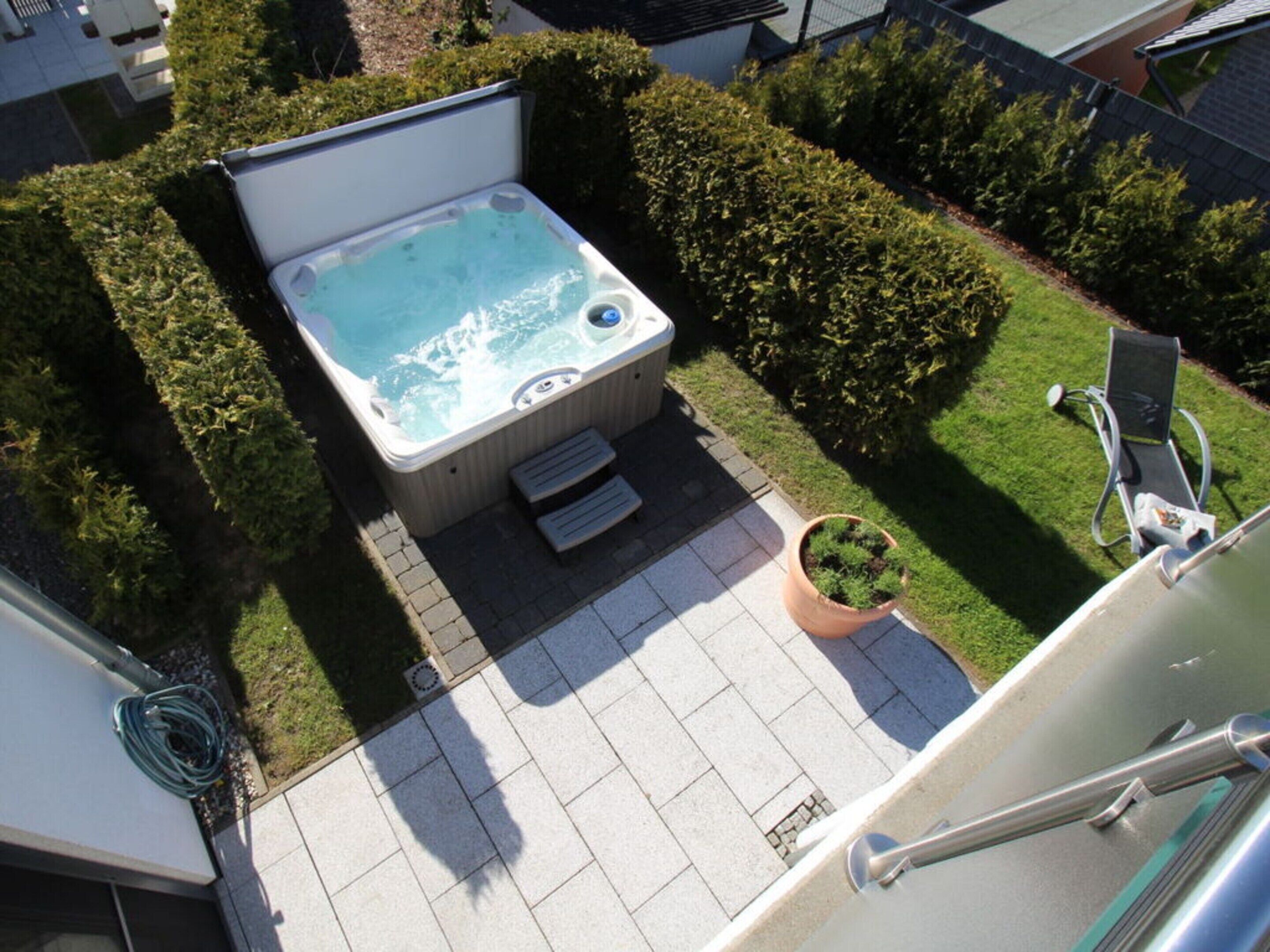 A hot tub in a backyard with a lawn chair and a potted plant.