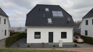 Une maison moderne à deux étages, dotée d’un toit en pente, d’un petit porche à l’avant et d’une voiture garée dans l’allée.