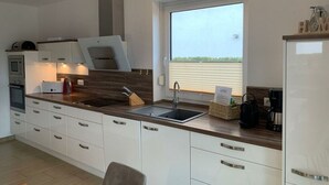 Une cuisine moderne avec des armoires blanches, un plan de travail en bois, un four encastré, un évier et une fenêtre donnant sur un paysage agréable.