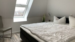 Une chambre à coucher moderne avec une lucarne, un lit recouvert de linge de lit blanc, une table de chevet et une chaise.
