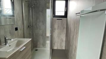 A modern bathroom with a glass shower enclosure, a sink with a mirror, and a window providing natural light.