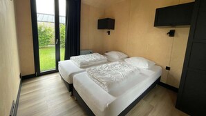 Habitación de hotel con dos camas, una puerta corrediza al exterior, un televisor de pantalla plana en la pared y suelo de madera.