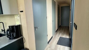 Un pasillo estrecho con una cafetera sobre una encimera, un cubo de basura y una puerta con manija.