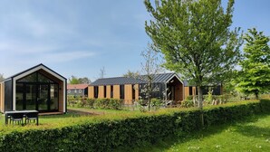 Una casa moderna con un amplio ventanal, una terraza de madera y un jardín cuidado.