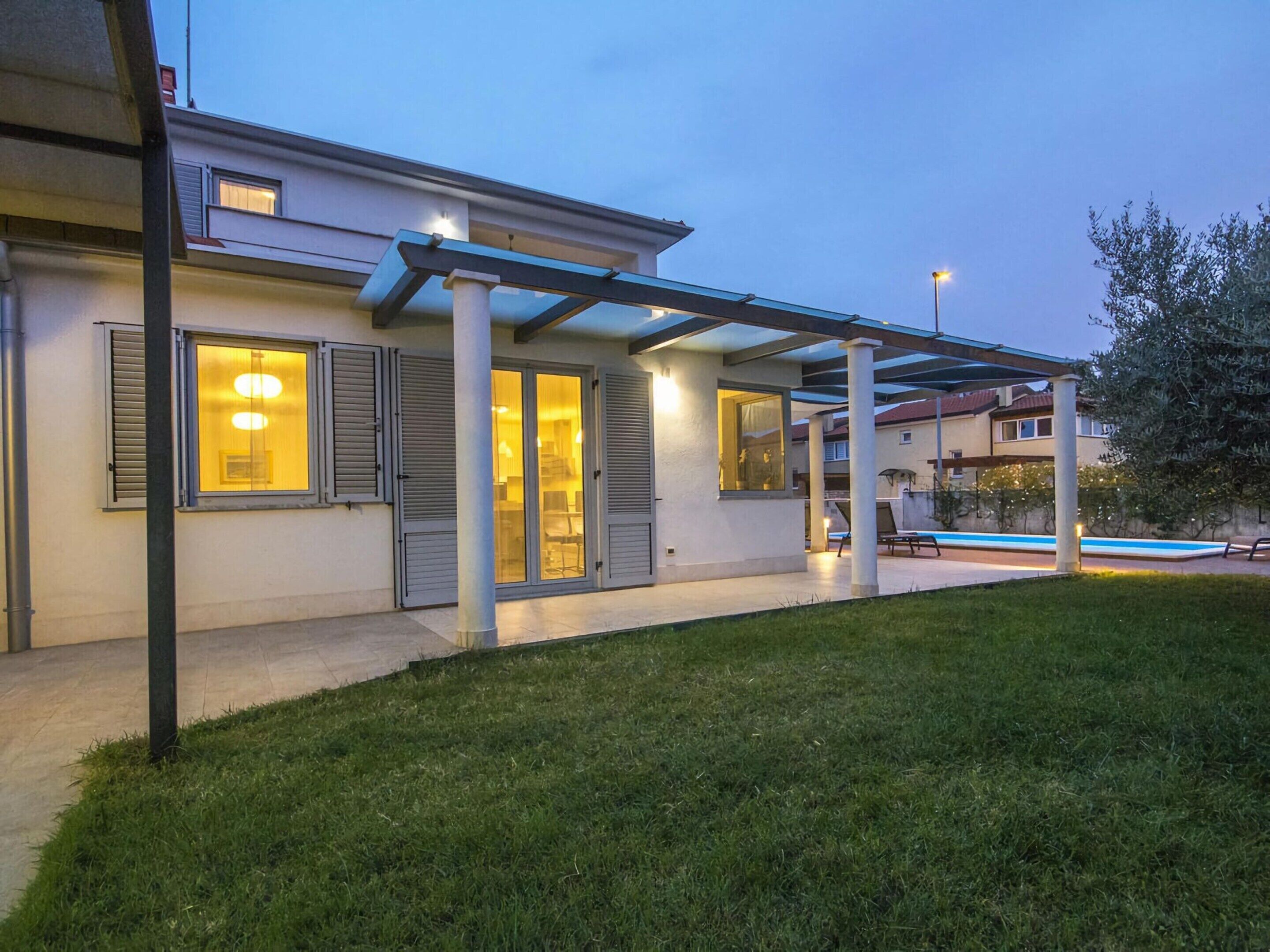 Une maison moderne dotée d’un patio couvert, d’une piscine et d’une pelouse bien entretenue.