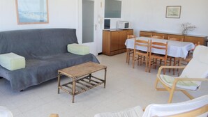 A living room with a grey sofa, a small table, wooden chairs, a dining table with a white tablecloth, and a kitchen area with a microwave. - Apartment in Nieuwpoort With Sea Views (Nieuwpoort)
