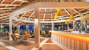 Un espacio interior amplio con piso de madera, techo alto con vigas a la vista y zona de bar con iluminación colgante amarilla.
