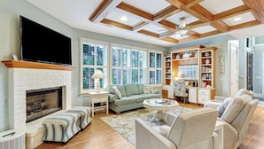 A spacious living room with a fireplace, comfortable seating, a television, and a large window with blinds. - 2 Genoa Court at The Sea Pines Resort (Hilton Head Island)