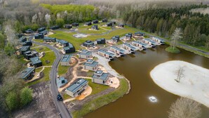 Vue aérienne d’un complexe hôtelier moderne et écologique, composé de plusieurs chalets disposés autour d’un plan d’eau central et reliés par des sentiers.