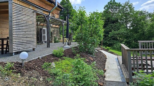 A modern building with a wooden exterior, a covered outdoor area, and a garden with a pathway. - Lovely Apartment in Rettenberg (St Andra-Hoech)