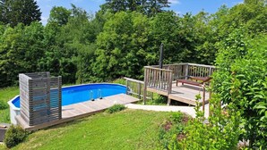 A backyard with a swimming pool, a wooden deck, and a grassy lawn surrounded by trees. - Lovely Apartment in Rettenberg (St Andra-Hoech)