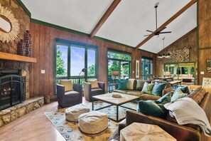 A spacious living room with a fireplace, large windows, and a ceiling fan. - Mountain Laurel Lodge in Big Canoe with mountain views and game room! (Jasper)