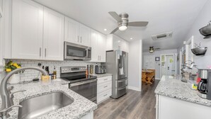 Eine moderne Küche mit weißen Schränken, Edelstahlgeräten, Granit Arbeitsplatten und einem Deckenventilator.