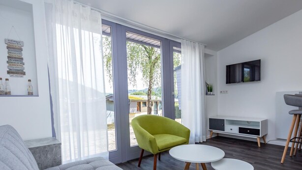 Un salon moderne avec un canapé gris, un fauteuil vert et deux petites tables rondes blanches.