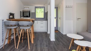 Un espace de vie compact comprenant un coin cuisine, un coin repas avec deux chaises, un canapé et une petite table.