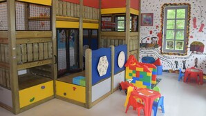 Une salle de jeux pour enfants avec des lits superposés, des structures de jeu et une fenêtre décorée d’œuvres d’art.