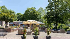 Un espace extérieur aménagé en terrasse, avec un sol en bois, des meubles pour s’asseoir et des plantes en pot.