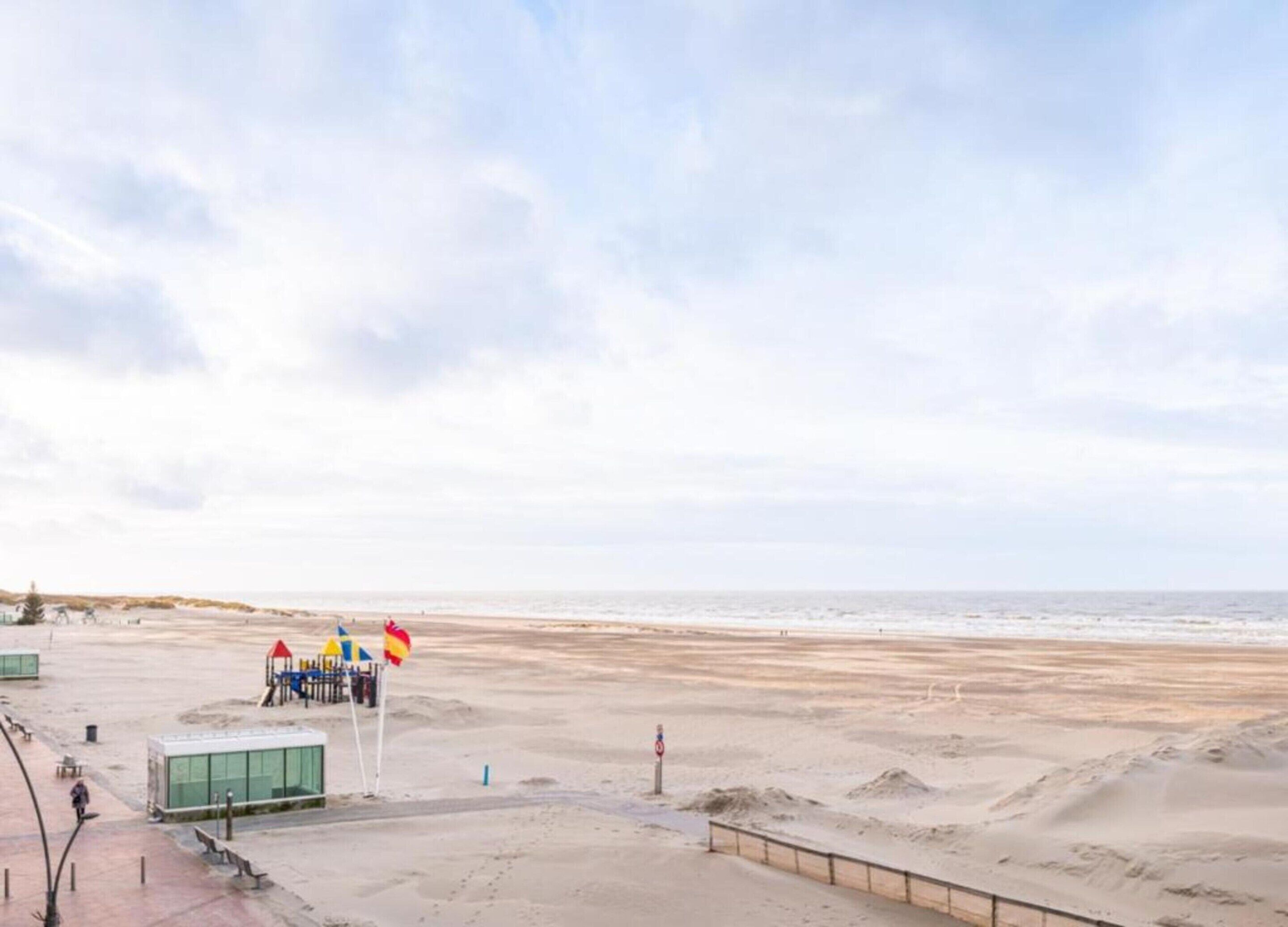 Een strand met een speeltuin en een klein gebouwtje, waarschijnlijk een redepost.