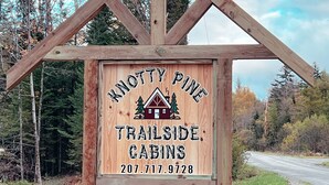 A wooden sign for Knotty Pine Trailside Cabins with a contact number. - Cabin 2 Recreational Cozy Cabin Rentals (Sangerville)