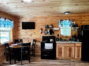 A wooden cabin interior with a dining table, chairs, a stove, a sink, and cabinets. - Cabin 2
Recreational Cozy Cabin Rentals (Sangerville)