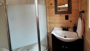 A wooden cabin bathroom with a glass shower enclosure, a white sink, and a mirror on the wall. - Cabin 2 Recreational Cozy Cabin Rentals (Sangerville)