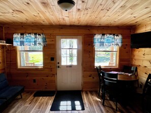A wooden cabin interior with a door, two windows with curtains, a sofa, a dining table with chairs, and a ceiling light fixture. - Cabin 2
Recreational Cozy Cabin Rentals (Sangerville)
