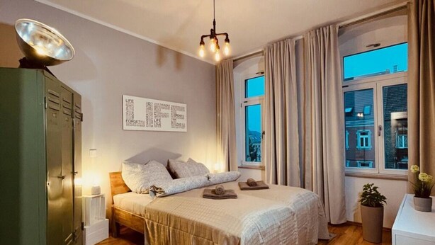 A bedroom with a bed, wooden floor, a wardrobe, a window with curtains, and a wall with a motivational quote. - Industrial Style Dresden (Dresden)